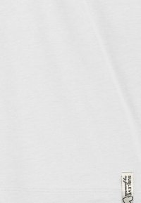 White cotton fabric with a smooth texture and subtle sheen, featuring a small woven label on the bottom right corner.
