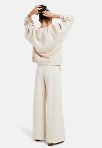 Beige oversized sweatshirt met geribde manchetten en zoom, gecombineerd met wijde beige sweatpants. Zachte stof met een gladde textuur.