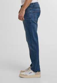 Blauwe denim jeans met een recht gesneden ontwerp, voor- en achterzakken en zichtbare stikdetails. Draagt met witte en beige sneakers.