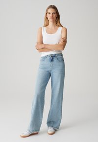 Jeans in denim di un azzurro chiaro a gamba larga con vita alta. Presentano un classico design a cinque tasche e una chiusura con bottone sul davanti.