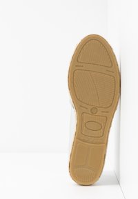 Semelle d'une chaussure marron clair avec un motif de grip texturé et une étiquette "Made in Spain" visible sur fond blanc.