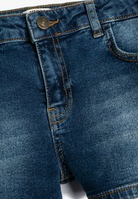 Jeans i denim i mörkblått med en lätt blekningseffekt. Funktionerna inkluderar orange sömmar, knap stängning och framfickor.