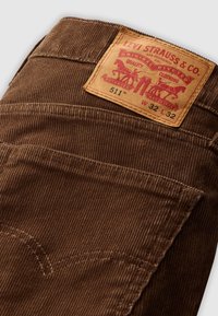 Jean en velours côtelé marron Levi’s 511 montrant la poche arrière et l’étiquette en cuir avec la marque, taille W32 L32 et logo aux deux chevaux.