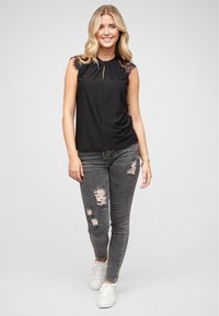 Haut sans manches noir avec des accents en dentelle aux épaules, détail en ouverture à la nuque ; associé à un jean foncé usé et des baskets blanches.