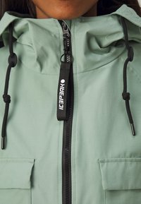 Veste vert clair avec un devant zippé, des cordons de serrage ajustables et deux poches avant, au toucher doux et au design minimal.