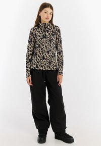 Dlhý rukáv, vysoký golier s leopardím vzorom v hnedých a čiernych farbách; skombinované s voľnými čiernymi nohavicami a čiernymi čižmami.