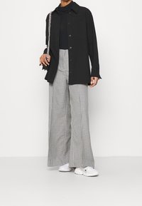 Svart skjorta med knappar, oversize passform, kombinerad med vida byxor i svart och vitt rutmönster. Vita sneakers och en kedjeväska ger detaljer.