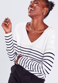 Pull rayé blanc et marine avec un col en V, comportant des rayures horizontales beiges et des boutons décoratifs sur l'épaule, texture en tricot douce.