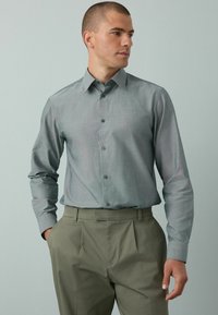 Hellgraues Hemd mit strukturiertem Kragen, langen Ärmeln und subtiler Textur, kombiniert mit hellen Khakihosen.