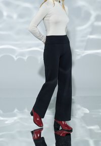 Pantalon rayé noir à jambes larges, associé à un col roulé beige ajusté et des chaussures rouges à talons carrés. Textures lisses visibles.