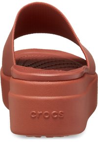 Des sandales à plateforme avec une finition rouge mate lisse, un dos ouvert et une large sangle supérieure. Présentent le logo "crocs" embossé sur le côté.