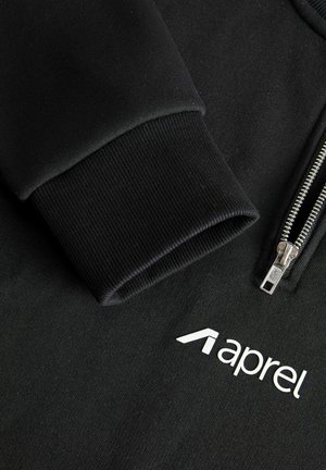Must kapuutsiga pusa, millel on siledast ja tekstuurse kangaga disain, soonikuga mansetid ning valge "aprel" logo rinnapiirkonnas.