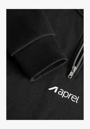 Musta vetoketjullinen huppari, jossa on sileä, teksturoitu kangas, resorit hihansuissa ja valkoinen "aprel"-logo rintakehän kohdalla.
