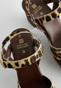 Sandale cu imprimeu de leopard, cu talpă din piele maro și curea la gleznă. Prezintă un toc masiv și detalii cu cataramă metalică.