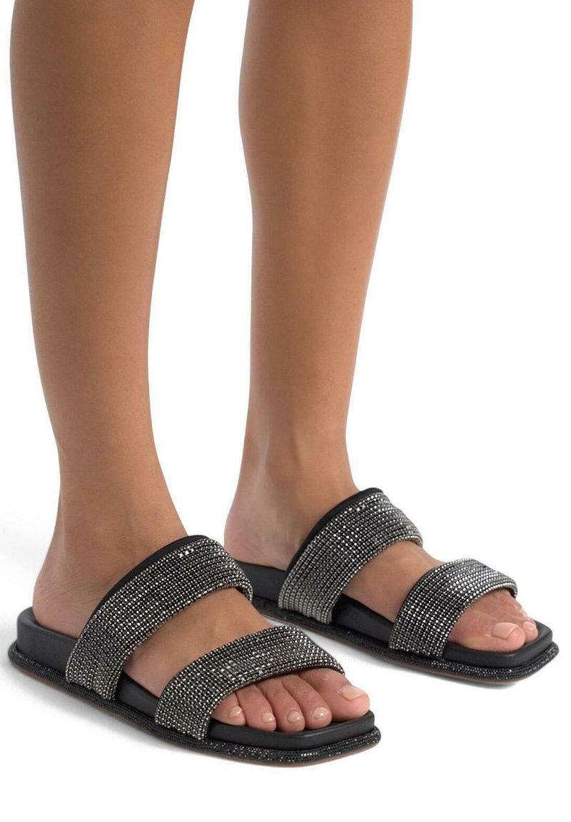 Sandales noires à semelle plate avec deux larges brides recouvertes de strass transparents. Semelle plate avec une surface texturée, laissant apparaître les orteils.