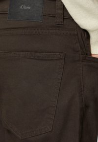 Braune Hose mit glatter Textur, ausgestattet mit einer Gesäßtasche, genähten Details und einem schwarzen Lederpatch mit der Aufschrift "s.Oliver."