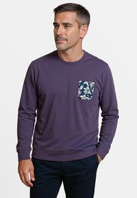 Paarse lange mouwenshirt met een marineblauw en witte bloemenzakdetail, ronde halslijn en geribbelde manchetten, gecombineerd met donkere broek.