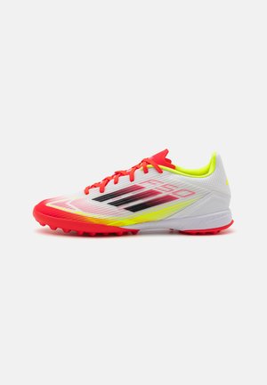 White soccer cleat with red and yellow accents, textured mesh upper, black stripes, and a durable sole with studded grip.