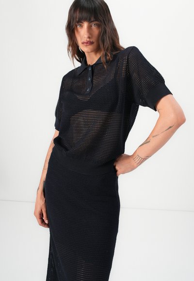 Polo shirt negru tricotat, cu mâneci scurte, având un design din plasă și un guler cu trei butoane. Asortat cu o fustă corespunzătoare.
