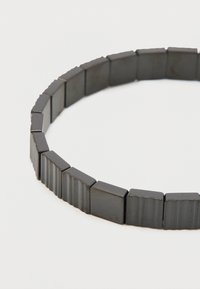 Black beaded bracelet featuring rectangular and ridged links, smooth texture, and a flexible design for comfortable wear.