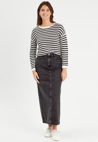 Striped black and white knitted sweater, paired with a high-waisted black denim skirt. Model wears white sneakers. Smooth textures, relaxed fit.