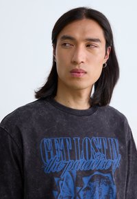 Grafisk sort T-shirt med blå tekst, der står "FORSVIND I paradisets" og detaljerede grafikker. Lavet af blødt, let slidte stof.