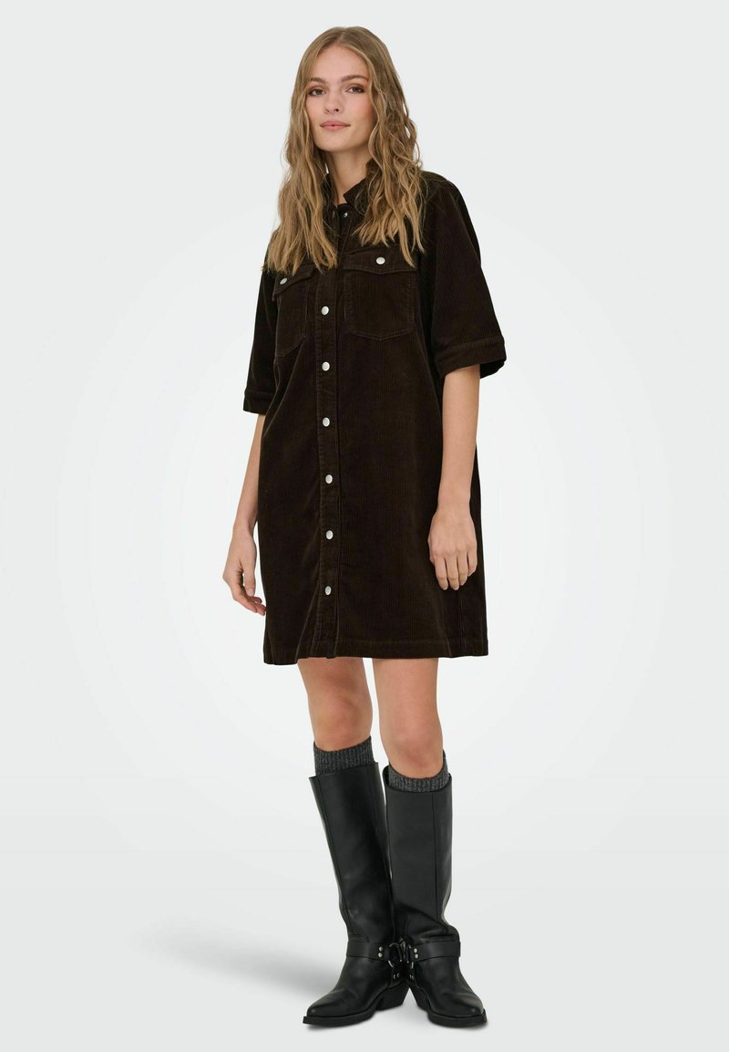 Brūna kordurova krekla kleita ar īsām piedurknēm, priekšpusē pogas, divām krūšu kabatām un vaļēju piegriezumu, kombinēta ar melniem ceļgalu augstiem zābakiem.