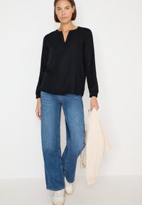 Blusa negra de manga larga con escote en V y costuras detalladas, combinada con vaqueros de pierna ancha de color azul claro y zapatillas blancas.