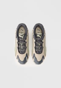 Pár béžovo-černých běžeckých bot Puma z prodyšného materiálu s šněrováním, zobrazený zeshora na bílém pozadí.