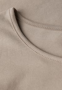 Ingrandimento di un tessuto di cotone beige che mostra le cuciture dettagliate attorno a un colletto arrotondato.