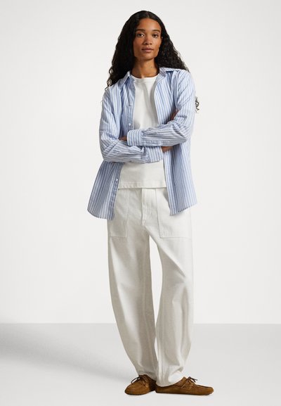 Ριγέ μπλε και λευκό πουκάμισο με κουμπιά πάνω από ένα λευκό μπλουζάκι με στρογγυλή λαιμόκοψη, συνδυασμένο με άνετο λευκό παντελόνι και καφέ μοκασίνια.