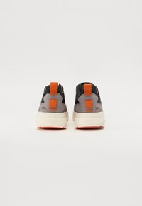 Baskets avec une tige en suède gris et en mesh, accents noirs, onglet de talon orange, et une semelle en caoutchouc léger avec un motif texturé.