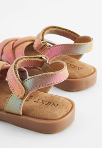 Sandali con cinturini dall'aspetto iridescente e lucido, dotati di una morbida soletta in suede e una suola in gomma marrone resistente. Regolabili tramite fibbie.