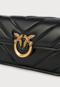 Μαύρη τσάντα χιαστί από καπιτονέ δέρμα, με χρυσή διπλή διακόσμηση που απεικονίζει πουλερικά και κυκλικό μεταλλικό στοιχείο. Η εμφάνιση σε σχέδιο chevron προσθέτει λεπτομέρεια.