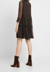 Svart lager-på-lager klänning med genomskinliga långa ärmar och ett blommönster. Buren med bruna klackkängor anklar med krokodilstruktur.