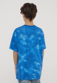 T-shirt blu tie-dye in cotone morbido. Presenta una vestibilità rilassata, maniche corte e scollo a girocollo con diverse sfumature di blu.