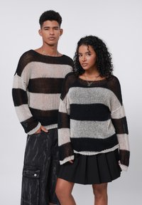 Maglioni knit a righe nere e crema con vestibilità ampia, scollatura larga e filato testurizzato. Abbinati a pantaloni scuri e una gonna nera plissettata.