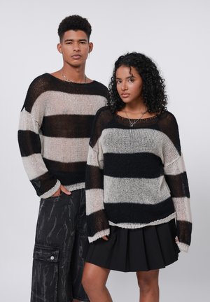Maglioni knit a righe nere e crema con vestibilità ampia, scollatura larga e filato testurizzato. Abbinati a pantaloni scuri e una gonna nera plissettata.