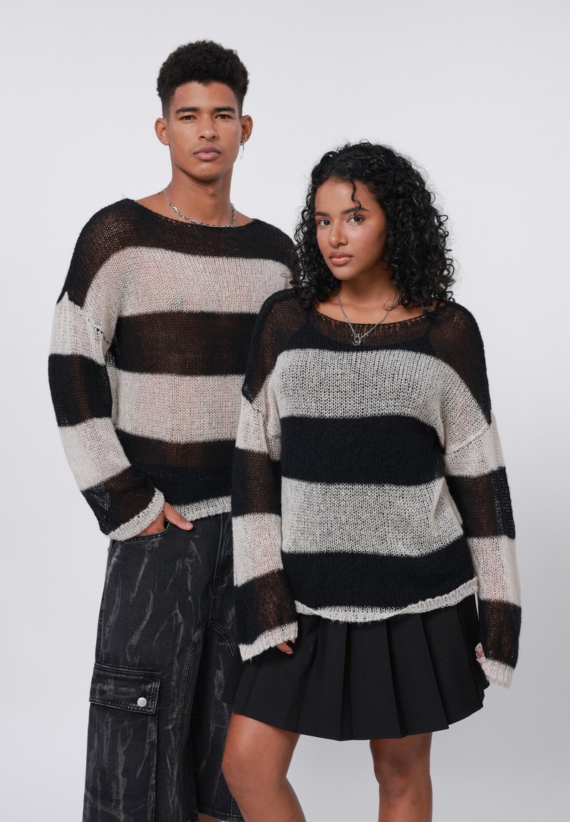 Maglioni knit a righe nere e crema con vestibilità ampia, scollatura larga e filato testurizzato. Abbinati a pantaloni scuri e una gonna nera plissettata.