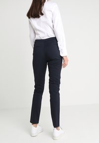 Granatowe spodnie slim-fit wykonane z gładkiego materiału, charakteryzujące się minimalistycznym wzornictwem i kieszeniami z przodu, zestawione z białymi trampkami i koszulą na guziki.