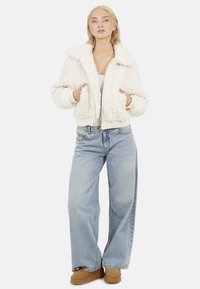 Crème-kleurige fluffy bomberjack met een brede kraag, geribde manchetten en zoom. Draag het met lichtblauwe high-waisted jeans en tan enkellaarsjes.