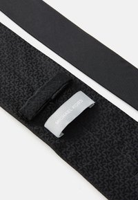 Centura neagră cu un model texturat, fabricată dintr-un material cu un finisaj neted. Include un eticheta dreptunghiulară cu "Michael Kors" în gri.
