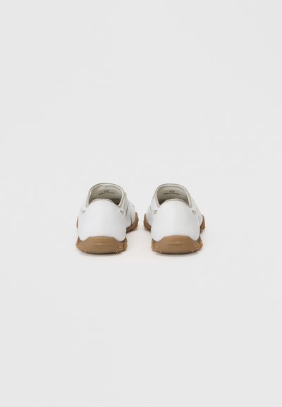 Chaussures blanches avec un matériau supérieur lisse, semelle en caoutchouc et un dessous texturé beige. Design slip-on sans quincaillerie ou accents visibles.