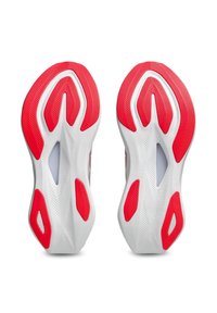 Semelles de chaussures de sport blanches et rouges avec des motifs de grip texturés et des sections découpées, montrées de dessous côte à côte.