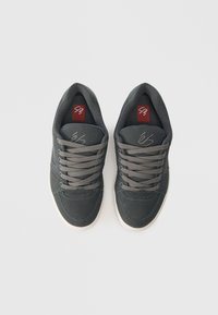 Σκούρο γκρι αθλητικά παπούτσια με υφή στην πάνω πλευρά, διαθέτουν γκρι κορδόνια, λευκές σόλες και διακριτές ραφές. Λογότυπο τυπωμένο στις σόλες.