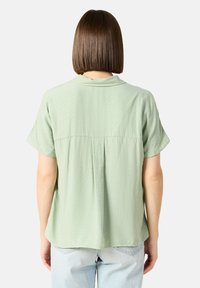 Korte mouwen, lichtgroen shirt van textuurstof met een subtiel ruitpatroon, voorzien van een kraag en een losse pasvorm.