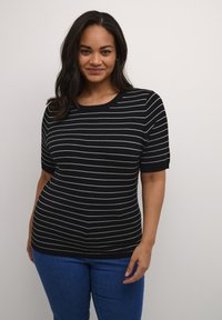 Maglione a righe bianco e nero con maniche corte, scollo rotondo e forma aderente. Abbinato a jeans di denim blu.