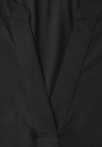 Gros plan sur un tissu noir avec un motif cousu en forme de V, probablement une partie du col ou du revers d'un vêtement.