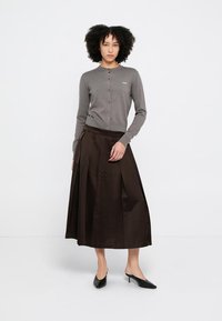 Cardigan grigio con scollo rotondo e chiusura con bottoni, abbinato a una gonna plissettata marrone scuro. Completa il look un paio di décolleté nere.