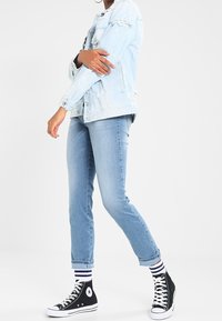 Ljusblå slitna denimjacka med lappar, tillsammans med medelblå slim fit-jeans och svarta högklackade sneakers med vita detaljer och randiga strumpor.
